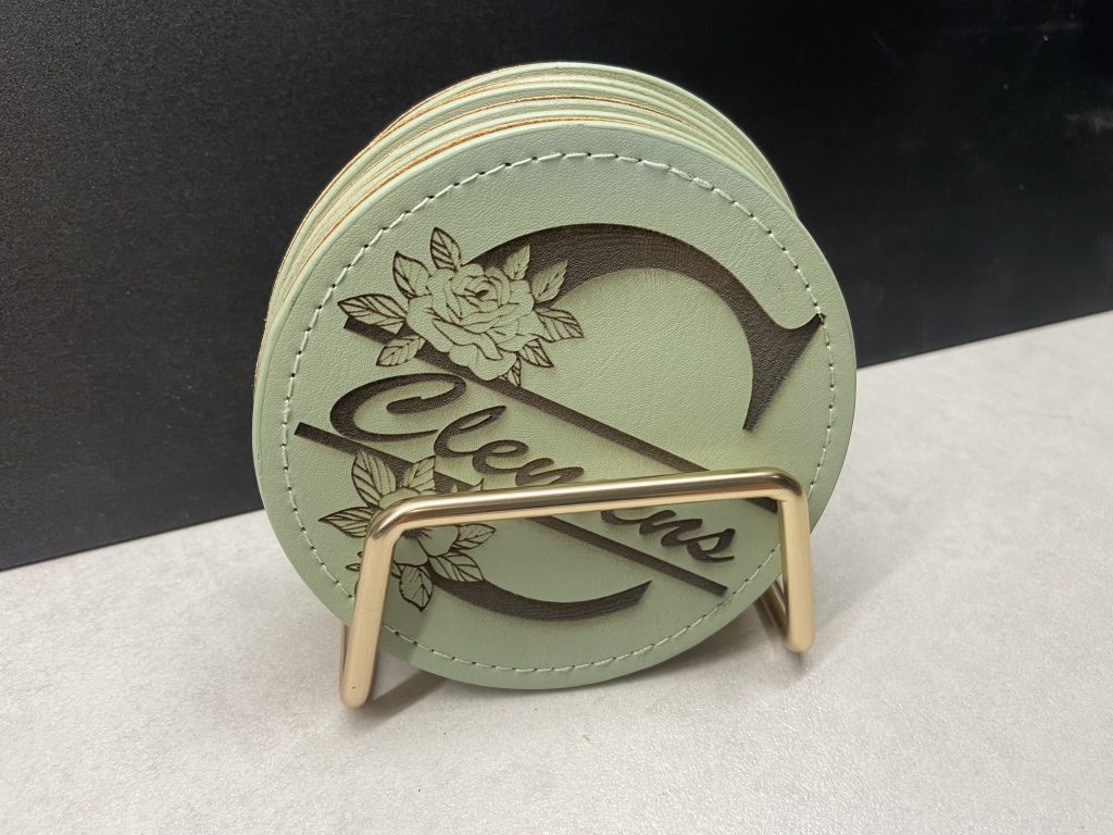 Runde Lederuntersetzer mit Namensgravur „Clemens“ und floralem Design im goldfarbenen Ständer.