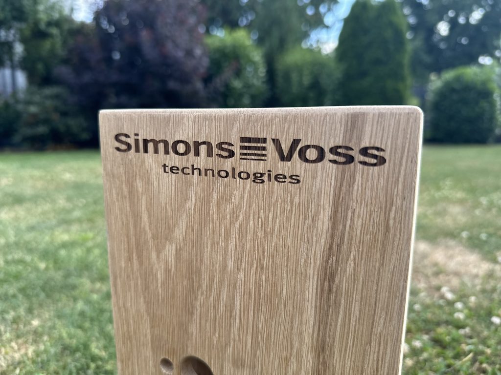 Lasergravur auf Holz – Logo von SimonsVoss technologies auf heller Holzfläche.