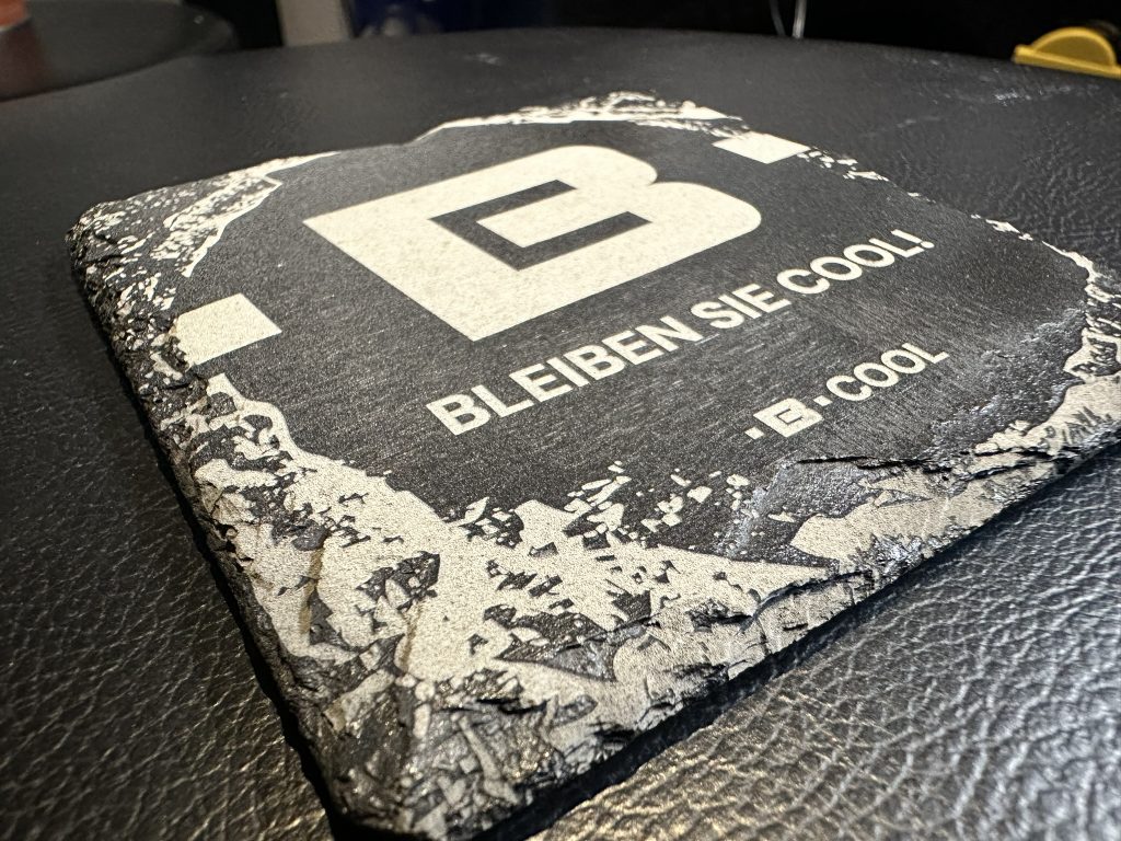 Schieferuntersetzer mit graviertem Logo und Schriftzug „BLEIBEN SIE COOL!“ – individuelles Werbegeschenk.