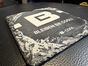 Gravierte Schieferuntersetzer mit Logo für Firmen Schieferuntersetzer mit graviertem Logo und Schriftzug „BLEIBEN SIE COOL!“ – individuelles Werbegeschenk.