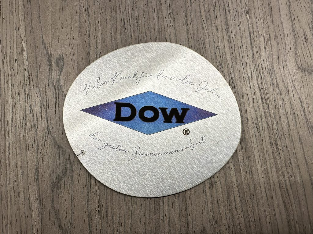 Gravierter Edelstahluntersetzer mit Dow-Logo und persönlicher Dankesbotschaft zur Zusammenarbeit.
